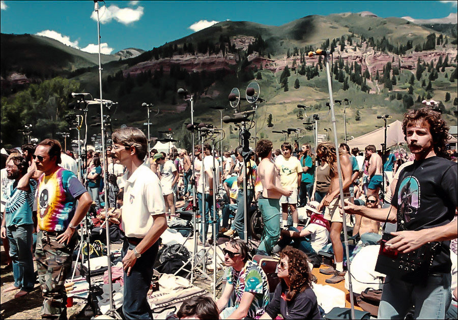 A crowd of people standing around dozens of microphones, recording an outdoor concert